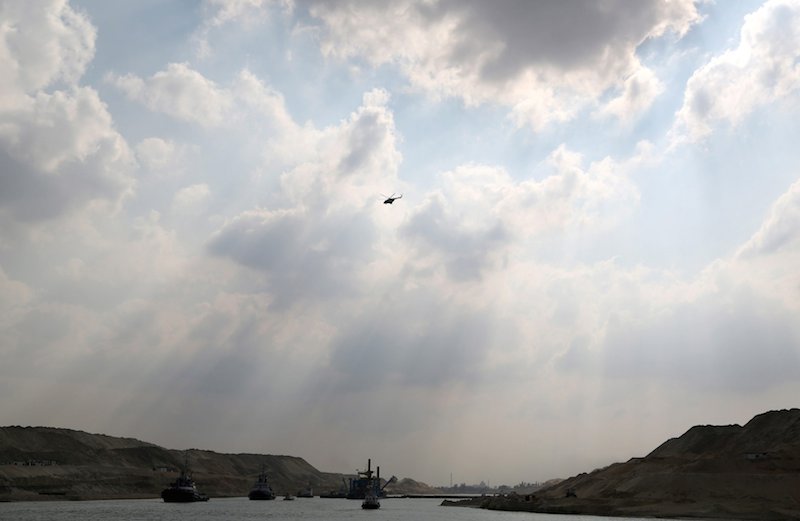 A military helicopter flies overhead as tractors and dredgers work on Egypt's new Suez Canal project at the Suez Canal zone Egypt